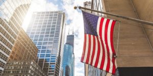 A photo of an American flag hanging outside downtown the city of Chicago with Sears Tower in the background.