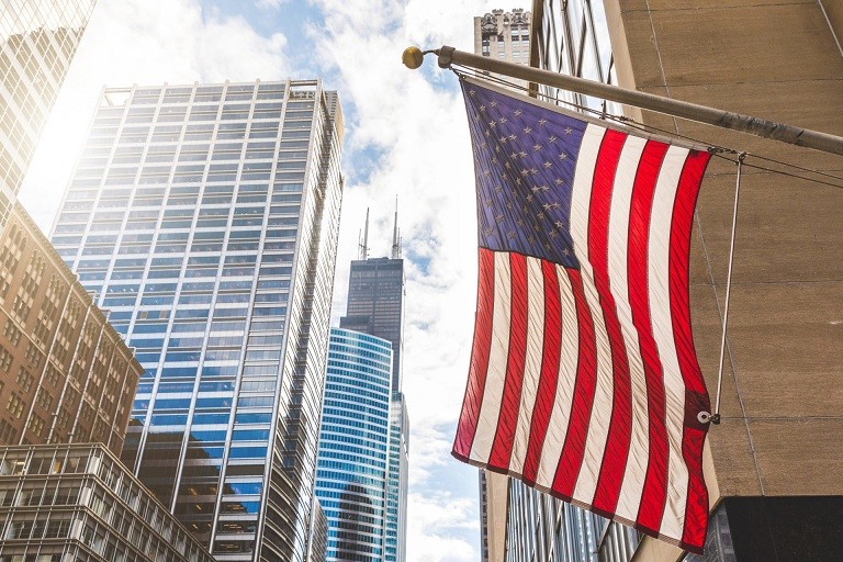 A photo of an American flag hanging outside downtown the city of Chicago with Sears Tower in the background.